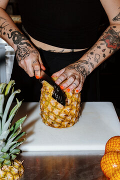 Cutting Fresh Pineapple With Tattooed Hands in a Vibrant Kitchen