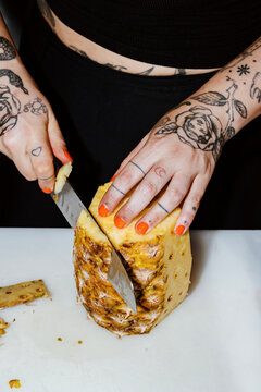 Cutting Fresh Pineapple With Tattooed Hands in a Vibrant Kitchen