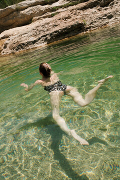 Woman swimming in clear green water at rocky natural pool