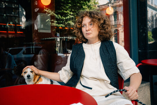 Woman Sitting at Cafe With Dog, Enjoying a Sunny Day Outside