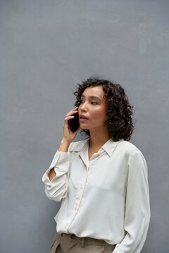 Woman talking on phone against a gray wall in a casual setting