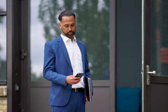 Businessman checking phone outside modern office setting