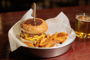 Juicy burger with cheese and golden fries served on a plate with a glass of beer on the table