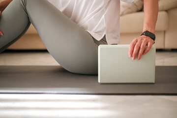 Naklejka premium Middle aged woman using yoga block during home workout on mat. Healthy lifestyle concept, fitness stretching, and pilates exercise at home.
