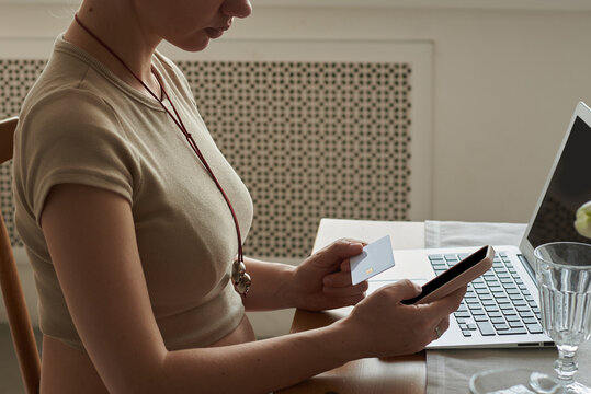 Woman sitting at a table using a smartphone and holding a credit card 