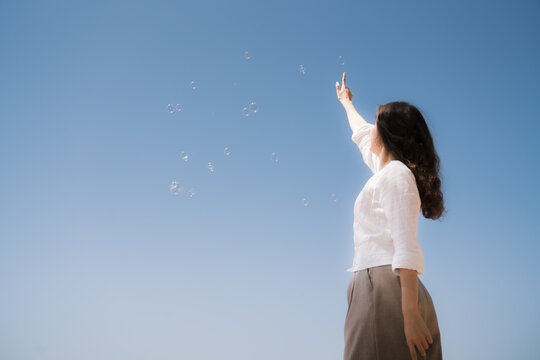 Woman reaching for bubbles in a clear blue sky