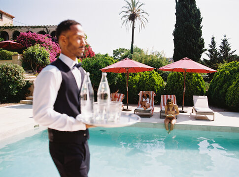 Waiter carrying drinks to tourists relaxing by hotel pool