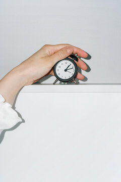 Hand turns off the ringing black alarm clock against a white wall.