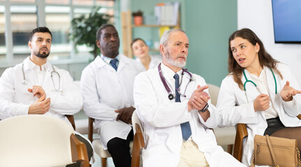 Eldery male doctor listening to lecture and watching presentation with colleagues in lecture hall
