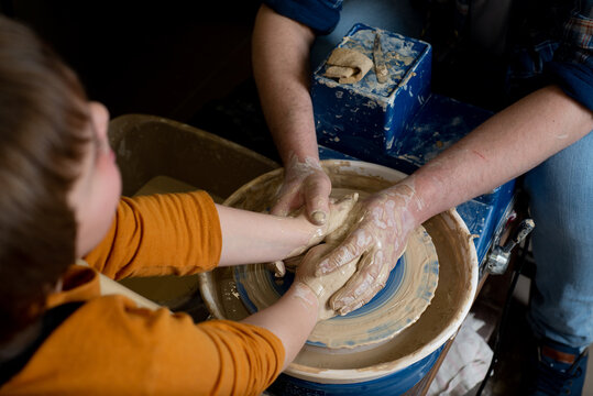 Faceless Master and a child make a clay plate on a potter's wheel