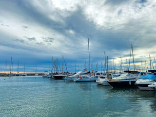 Obraz premium Boats are docked in a marina with cloudy skies above and calm waters during the late afternoon near the coast