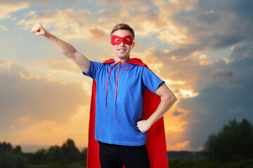 Man wearing red cape and face mask against beautiful sky at sunset. Super hero power in everyday life