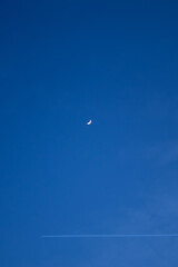 Crescent moon in deep blue twilight sky with airplane trail