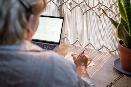 Woman Working on a Laptop While Writing Notes at Home