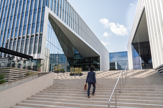 Businessman Walking up Stairs Towards Modern Office Buildings
