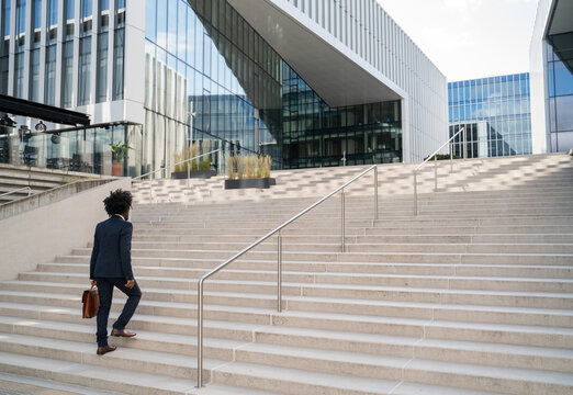 Businessman Walking up Stairs Towards Modern Office Buildings