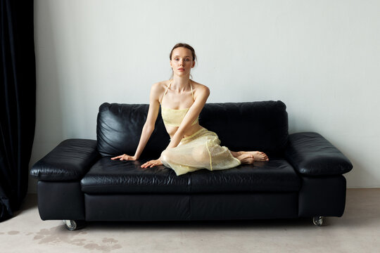 A girl sitting on a black leather sofa.