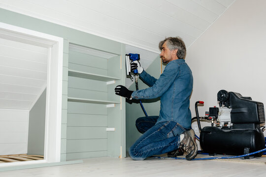 Handyman installing built-in shelving with pneumatic nail gun 