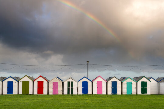 UK, England, Devonshire, Paignton.  A row of colourful  changing huts at the beach, with rainbow overhead.