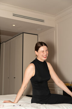 Smiling Woman in Black Dress Sitting on Hotel Bed
