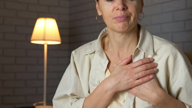 Mature woman touching her chest experiencing heart pain. Unhealthy middle-aged woman suffering from heart attack symptoms, putting her hand on her chest and experiencing pain while sitting alone