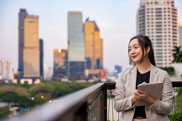 Luxury young Asian business woman entrepreneur using digital tablet while walking in the green building modern office downtown on background for communication and urban lifestyle