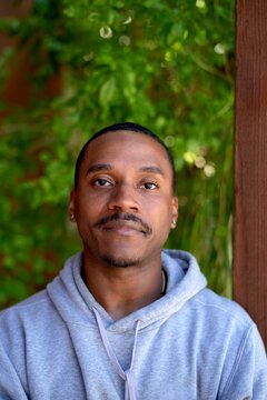 Smiling Man in Gray Hoodie Against Lush Greenery Backdrop