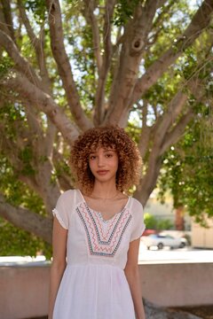 Young Woman Standing Under a Large Tree on a Sunny Day