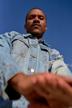 Man in Denim Jacket Poses Confidently Under Clear Blue Sky