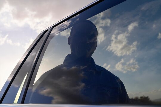 Reflections of Clouds and a Silhouette Through a Car Window
