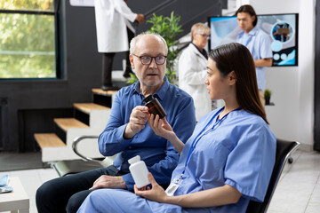 Obraz premium Senior man gets medical consultation guidance on pills, dosage and recovery steps from female nurse in clinic. Patient and healthcare worker discussing possible side effects of prescribed medicine.