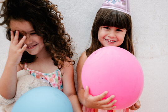 Two young sisters smiling with balloons while laughing at a party