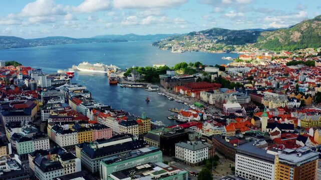 Establishing shot of Bergen harbor with a mix of historic UNESCO landmarks and modern urban architecture. Large cruise ships docked at the terminal with the city fjord. 4k aerial panorama 