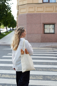 Woman crossing a street carrying a tote bag with fresh bread