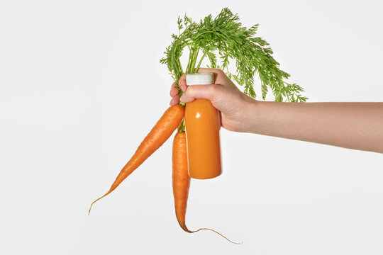 Hand holding Fresh Carrots and a Bottle of Orange Smoothie