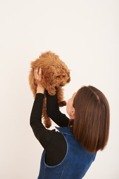 Woman joyfully holds a fluffy dog against a  white wall