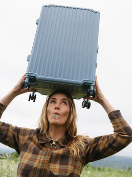 Woman Balancing Suitcase Outdoors in a Green Field