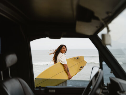 Surfer Carrying Yellow Boards Near Ocean on a Cloudy Day