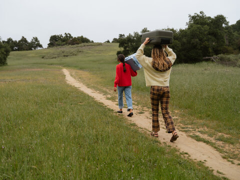 Two Friends Carry Suitcases Along a Grassy Path in Nature