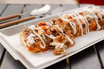 Long rectangular pizza topped with meat and mayo served with a layered purple lime drink on a black cafe table. Delicious modern fusion meal