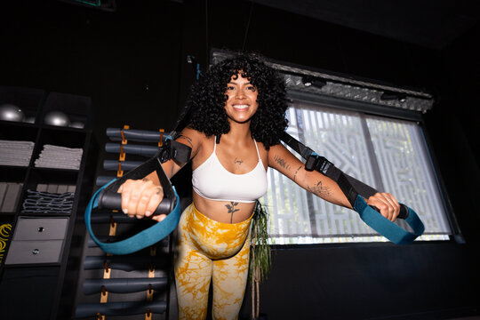 Pregnant woman doing fitness exercises with trx straps at gym