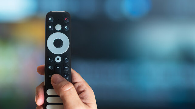 Hand using a modern TV remote control with copy space on a TV background, smart home technology concept