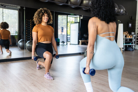 Two fitness instructors performing lunges with dumbbells in a gym