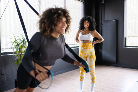 Fitness instructor assisting woman using suspension training straps