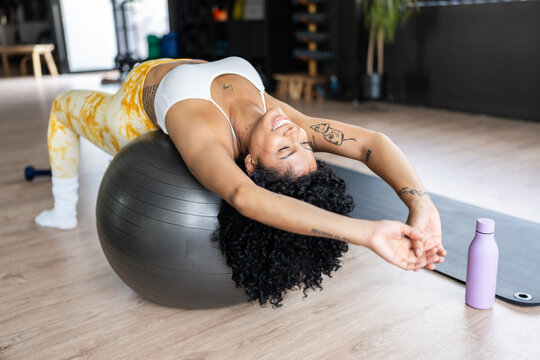 Young woman stretching back on fitness ball in gym enjoying workout