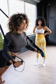 Pregnant personal trainer assisting woman exercising with trx straps