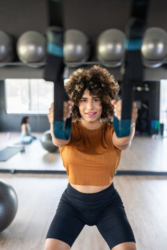 Sportswoman doing squats using suspension straps in a gym