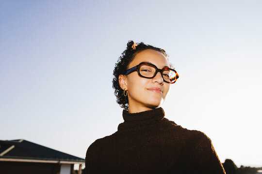 Confident woman in glasses poses under bright sky outdoors