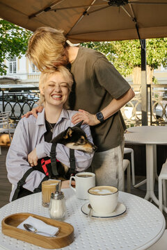 A guy kisses his smiling girlfriend with a dog in a summer cafe