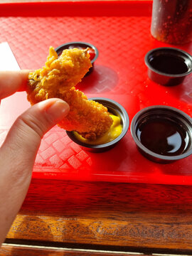 Person dipping fried chicken wing in mustard